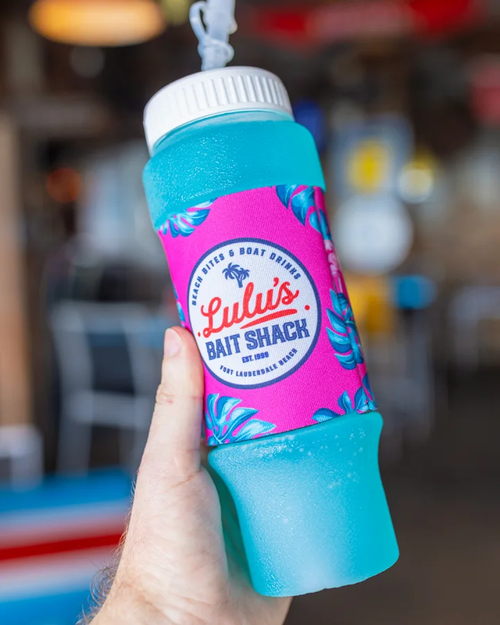 Blue frozen drink in a Lulu's branded souvenir squeeze bottle held inside the restaurant.